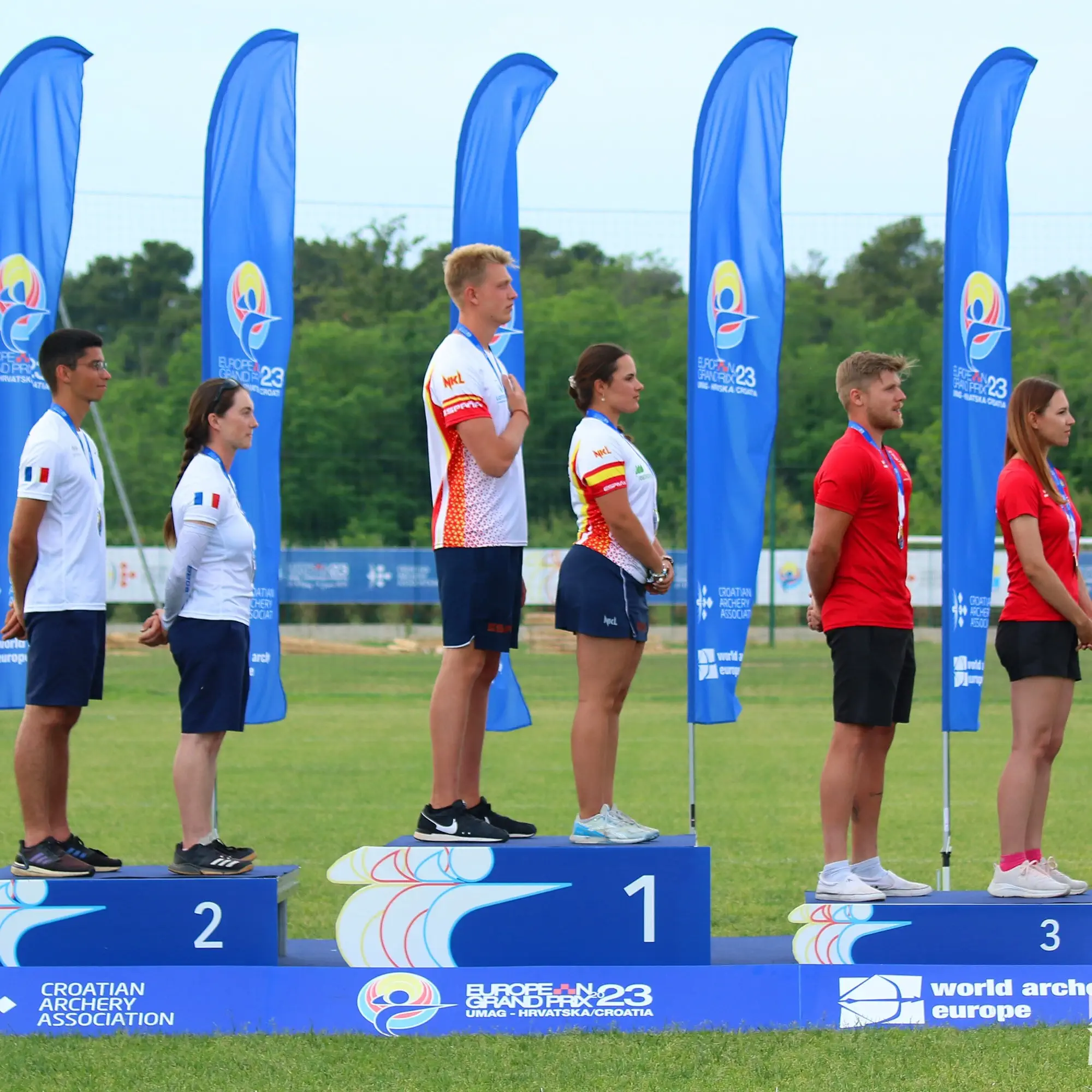 Javier Mérida y Elia Canales en lo alto del podio tras ganar la Copa de Europa de Tiro con Arco 2023 en Umag, Croacia, escuchando el himno nacional de España.